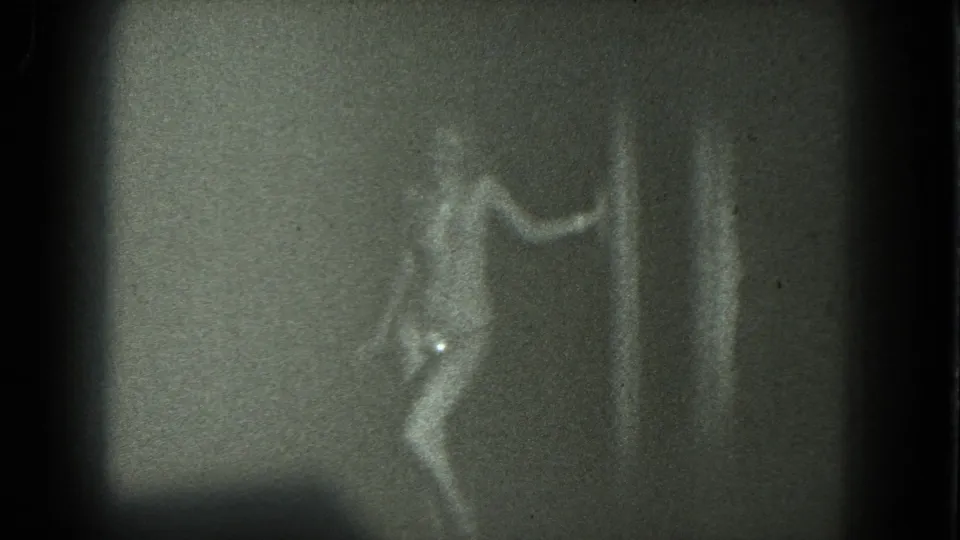 1975 San Francisco 8mm frame showing the dancer bent at the knees with one arm extended in a dim, shadowed room.