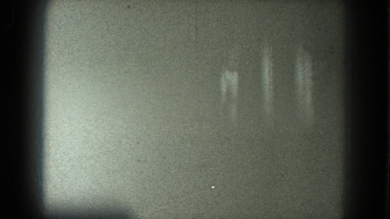 In supplied 1975 San Francisco 8mm footage, a scantily clad adult woman appears blurred under low stage lighting with her arms raised.