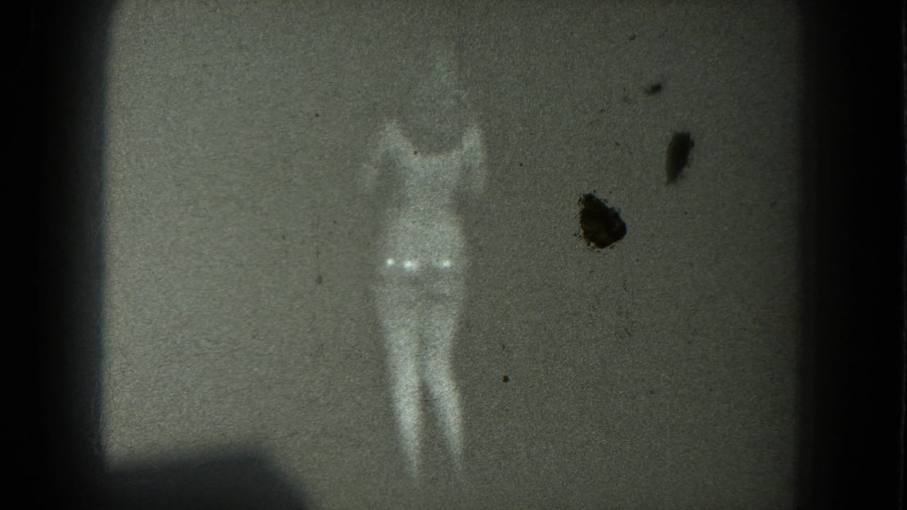 Scantily clad woman standing on a dark stage with arms lifted.