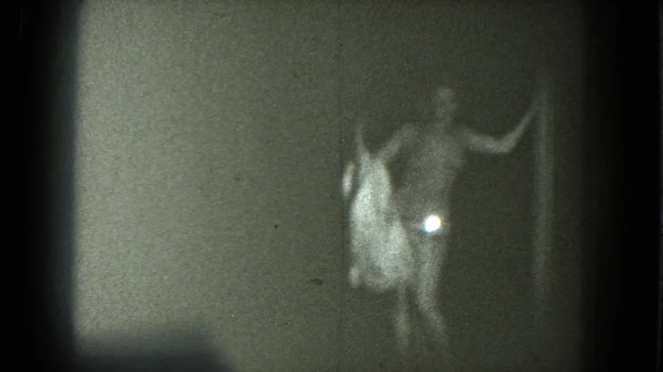 A scantily clad adult woman holds a pale cloth at her side while moving across the dark stage in the supplied 1975 San Francisco clip.