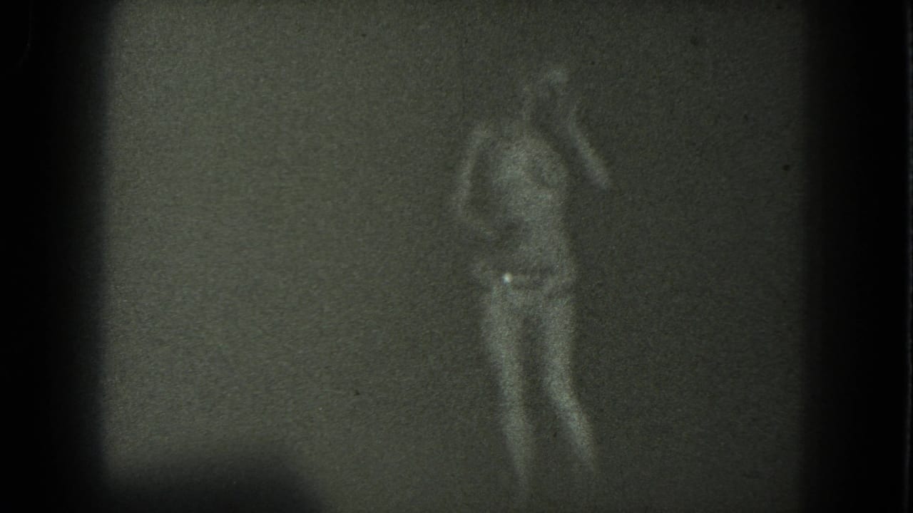 A grainy 1975 San Francisco frame shows an adult dancer in profile, arms lifted, wearing a long skirt against a bare wall or screen.