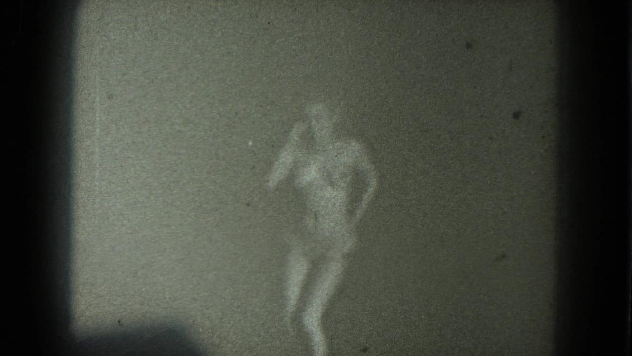 1975 San Francisco 8mm frame of a nude adult woman dancing in low light, her figure blurred by grain and soft focus.