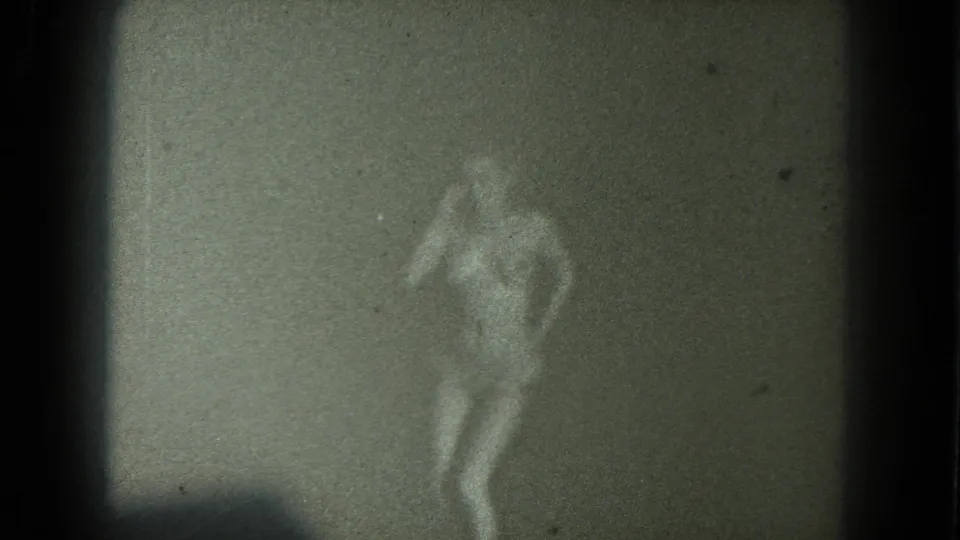 1975 San Francisco 8mm frame of a nude adult woman dancing in low light, her figure blurred by grain and soft focus.