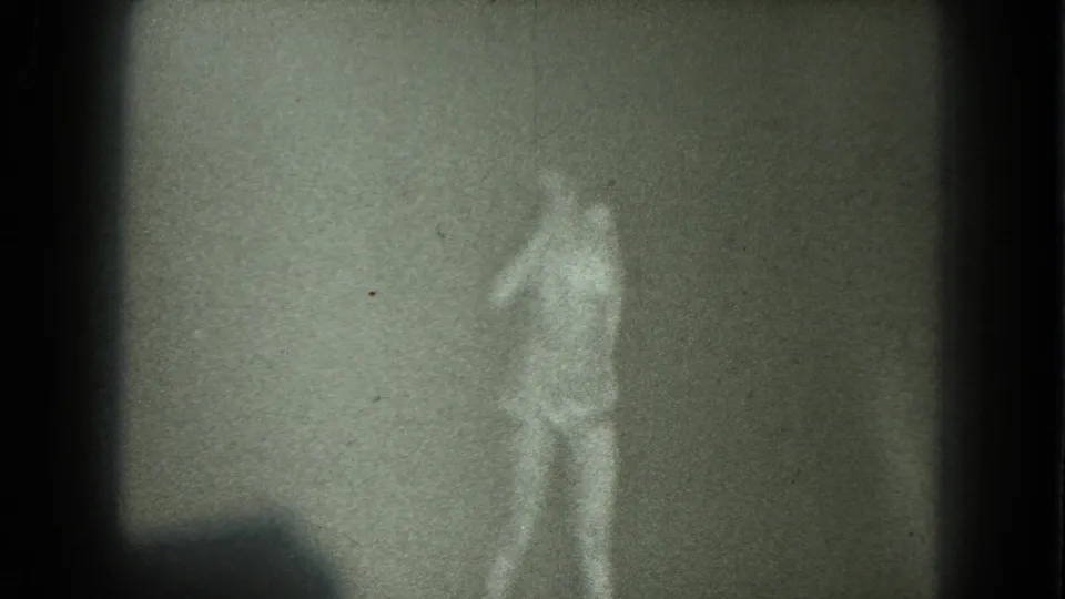 1975 San Francisco 8mm frame showing a nude adult woman in a low-lit interior, partially obscured by blur, grain, and shadow.