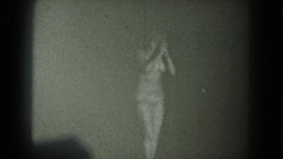 1975 San Francisco 8mm frame of a nude adult woman dancing near the edge of the frame, softened by low light and film grain.