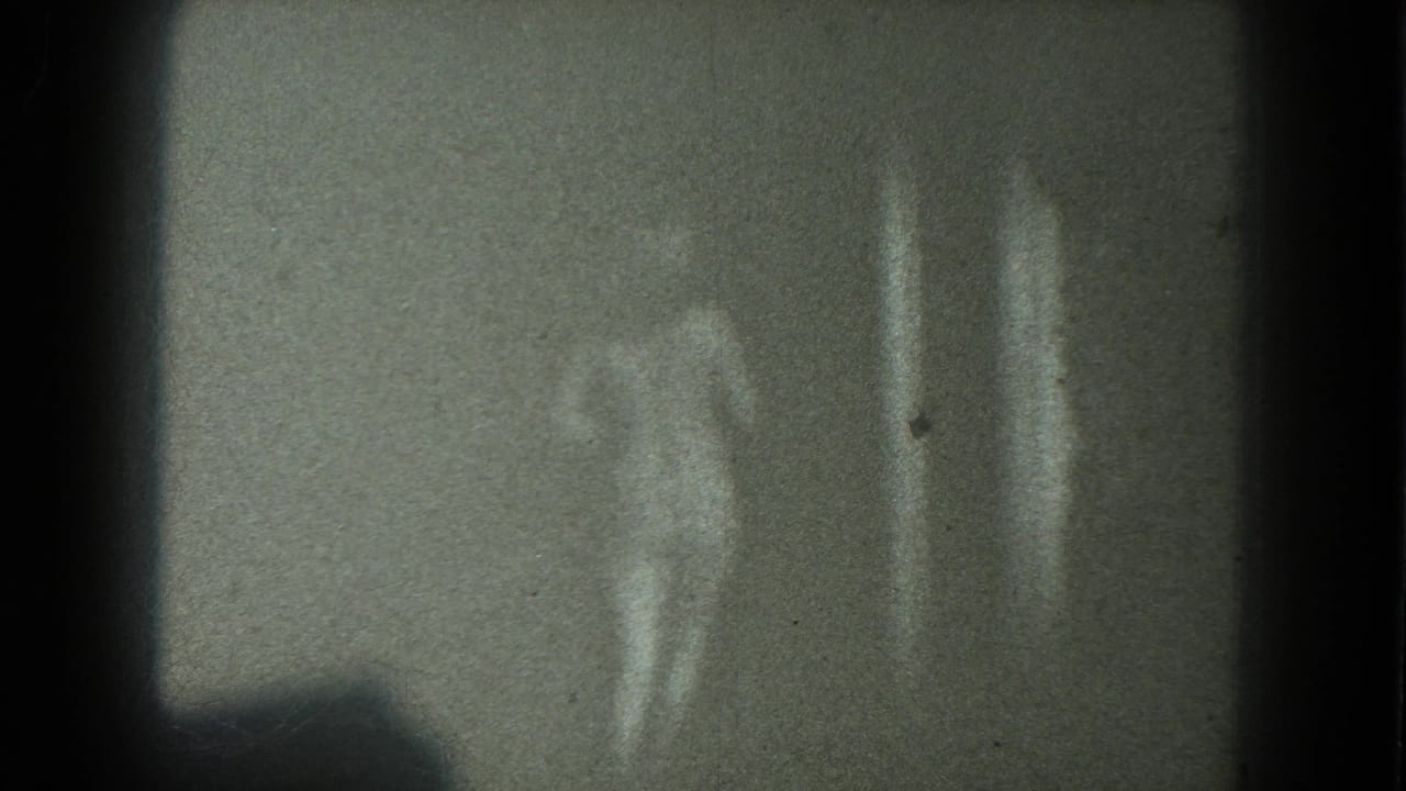 Two adult women appear near a plain wall in low-light 1975 San Francisco 8mm home-movie footage.