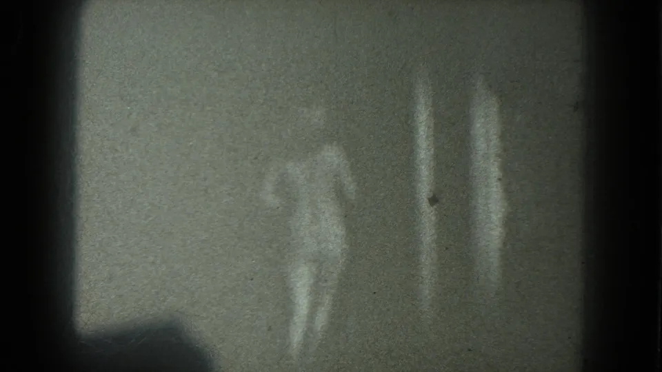 Two adult women appear near a plain wall in low-light 1975 San Francisco 8mm home-movie footage.