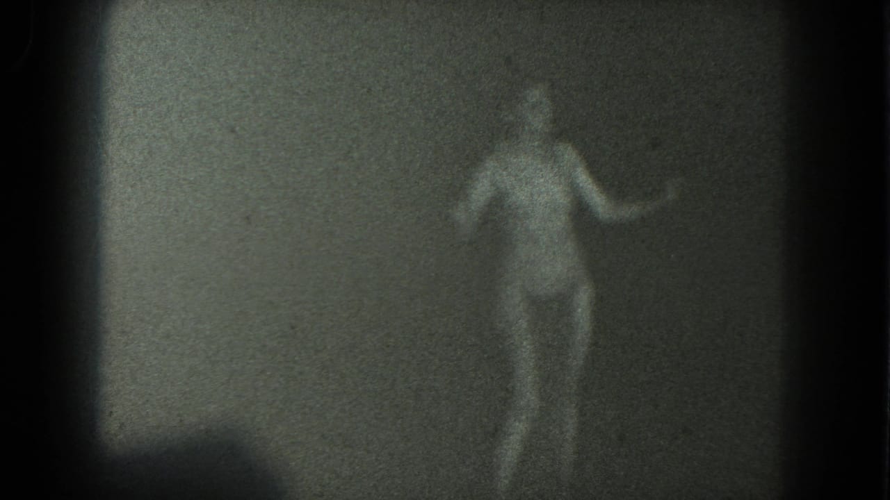 An adult woman in a two-piece bathing suit dances beside a plain wall in grainy 1975 San Francisco home-movie footage.
