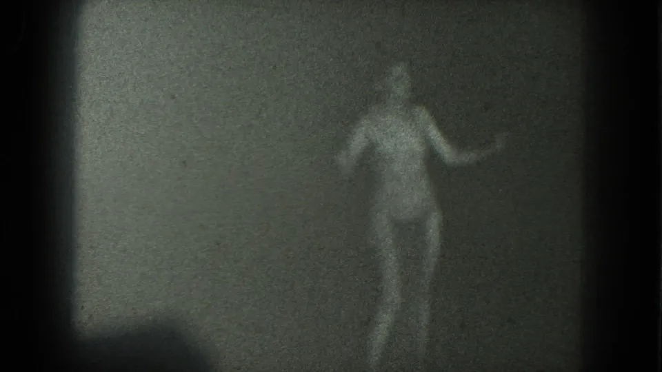 An adult woman in a two-piece bathing suit dances beside a plain wall in grainy 1975 San Francisco home-movie footage.