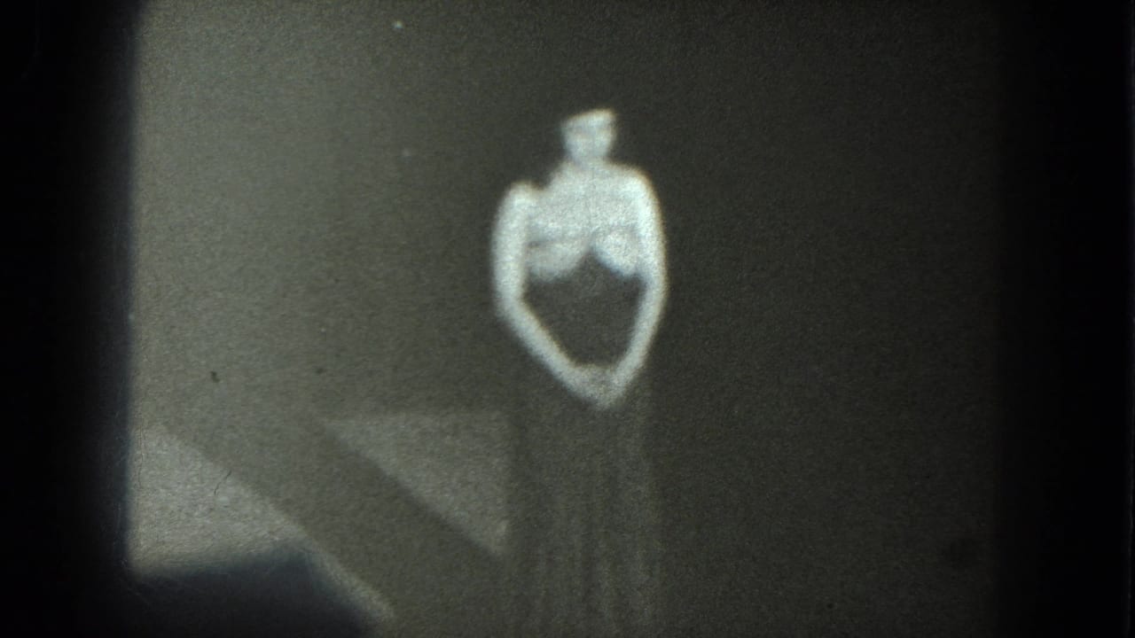 Woman in a dark form-fitting outfit stands against a plain dark backdrop.