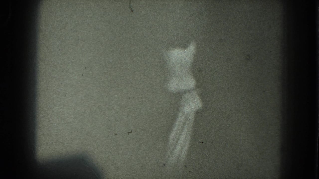 The dancer remains partially turned away in low light, with the 8mm frame showing muted tones, dust, and visible gate edges.