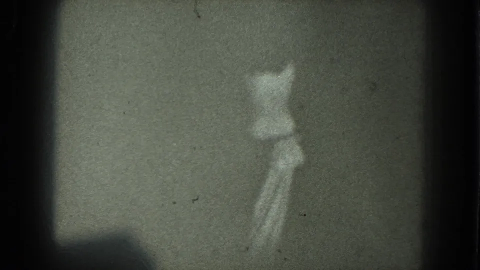The dancer remains partially turned away in low light, with the 8mm frame showing muted tones, dust, and visible gate edges.