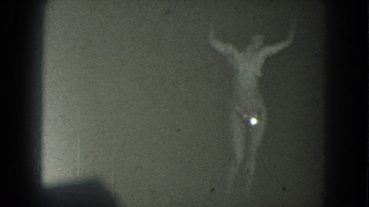 1975 San Francisco 8mm frame with a dim topless adult performer, raised arms, and a bright flare near her side.