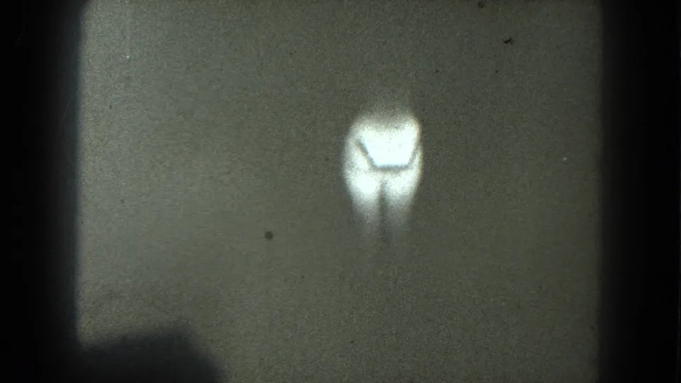A low-light 8mm frame from the 1975 San Francisco clip, showing a bright lamp-like flare below the dark backdrop.