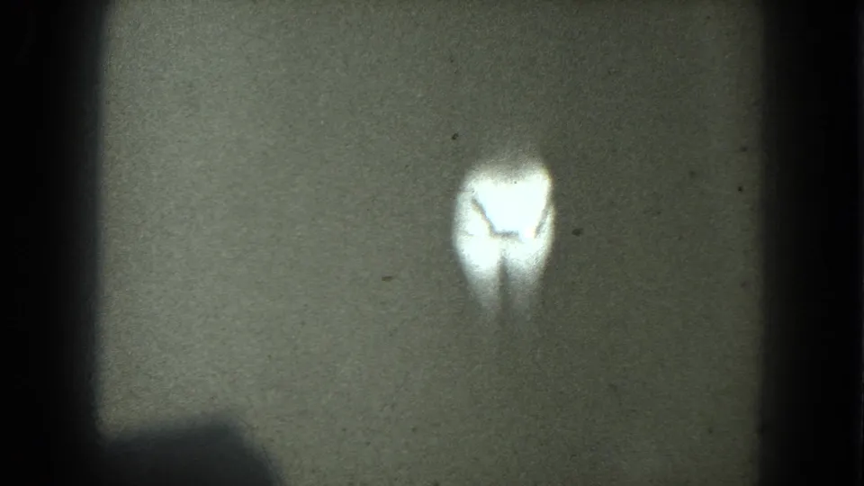 1975 8mm frame from metadata-described San Francisco footage showing a bright, indistinct dancer-like silhouette in a dark projected frame.