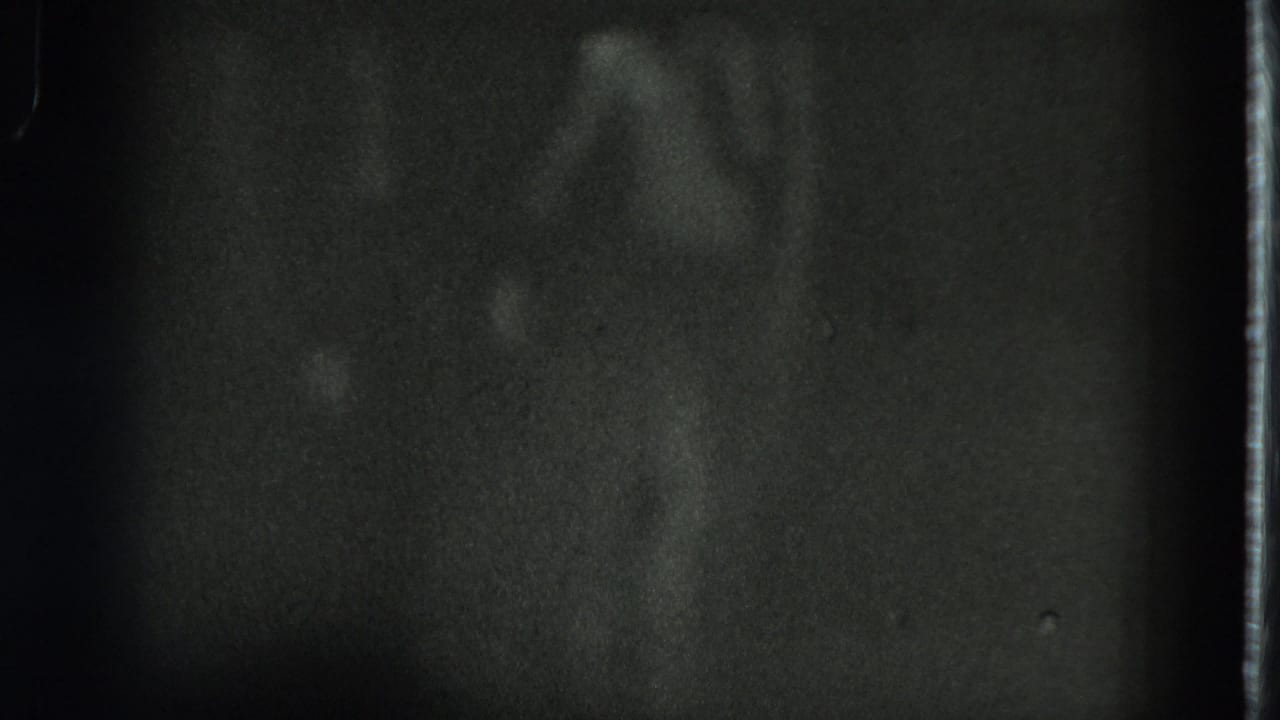 A faintly lit dancer in a grass skirt appears in dark 1975 San Francisco 8mm home-movie footage.