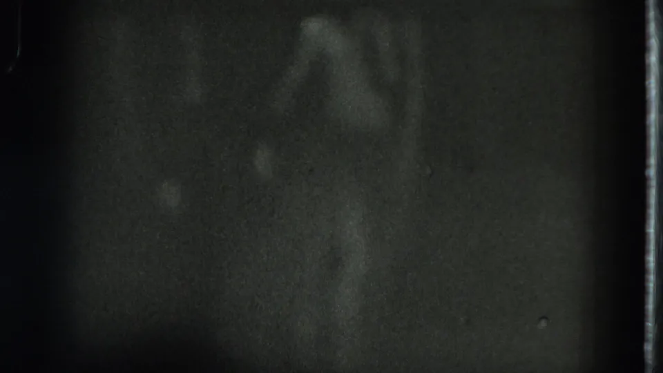 A faintly lit dancer in a grass skirt appears in dark 1975 San Francisco 8mm home-movie footage.