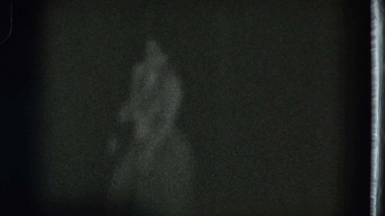 Very dark 1975 San Francisco 8mm frame with a barely visible performer standing against a dim background.