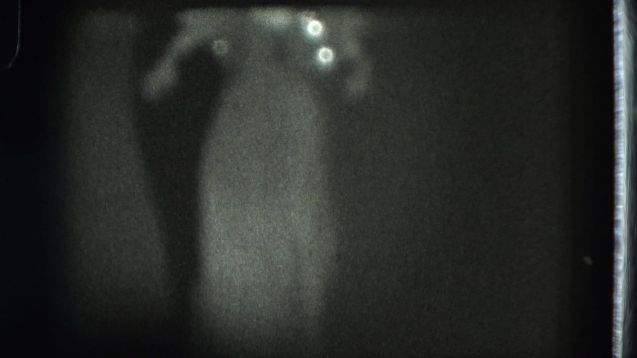 1975 San Francisco 8mm frame showing a soft, distant silhouette of a woman in a long dress under stage lighting.