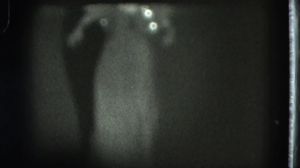 1975 San Francisco 8mm frame showing a soft, distant silhouette of a woman in a long dress under stage lighting.