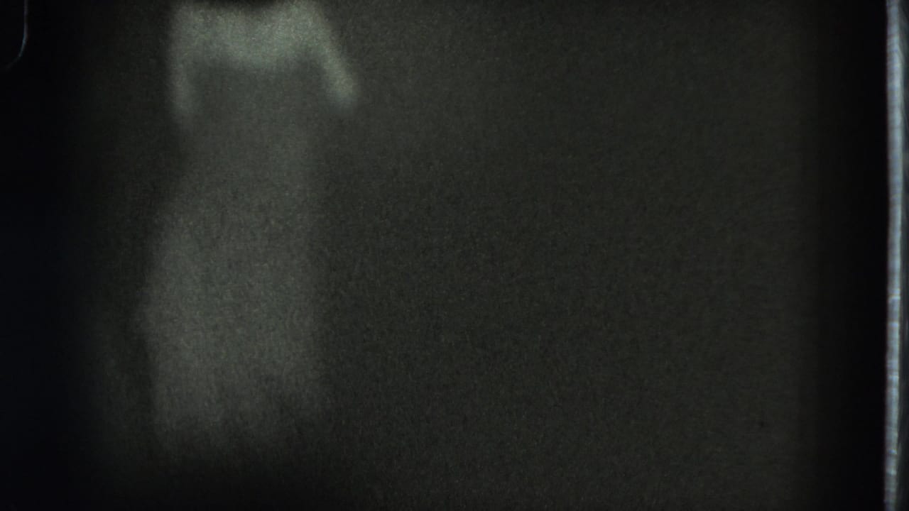 Grainy 1975 8mm frame from San Francisco showing a barely visible adult woman moving in a dark interior.