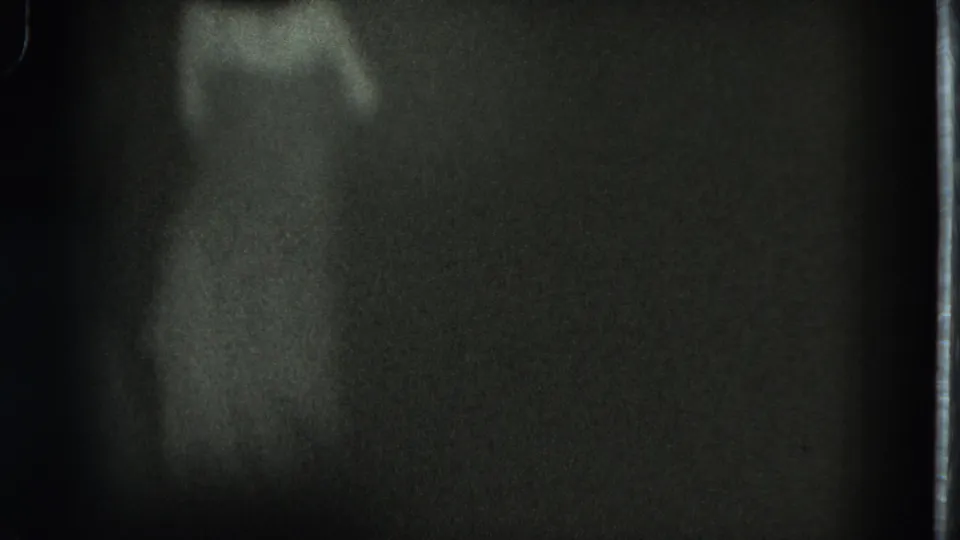 Grainy 1975 8mm frame from San Francisco showing a barely visible adult woman moving in a dark interior.