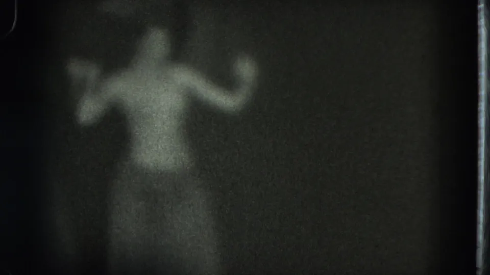 Grainy San Francisco home-movie frame shows the adult figure swaying with one arm raised in a dark room.