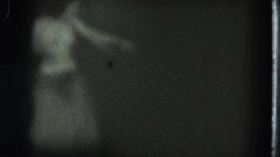 Soft black-and-white 1975 San Francisco home-movie frame showing a blurred adult figure with an arm raised in a dark room.