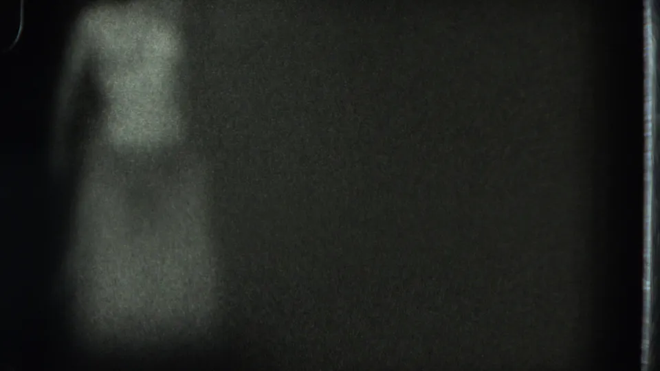 Grainy 1975 San Francisco home-movie frame with a faint adult figure standing or dancing in low light.