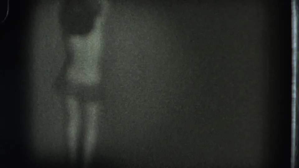 Low-light 1975 San Francisco 8mm frame with a soft rear view of an adult figure and visible film border.