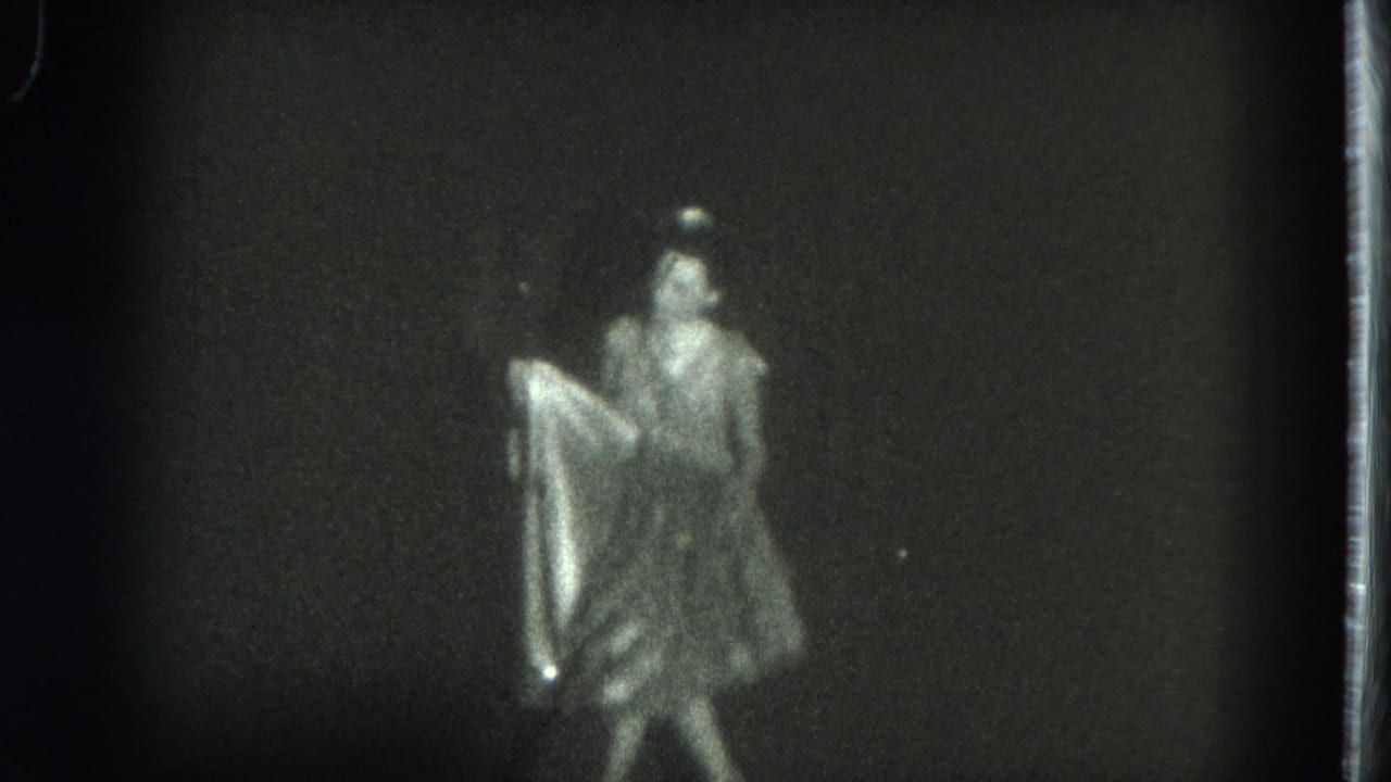 1975 San Francisco 8mm frame showing a female dancer in a light costume handling a flowing skirt against a dark backdrop.