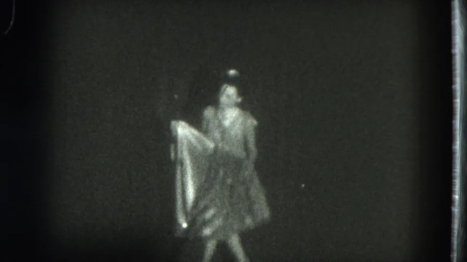 1975 San Francisco 8mm frame showing a female dancer in a light costume handling a flowing skirt against a dark backdrop.