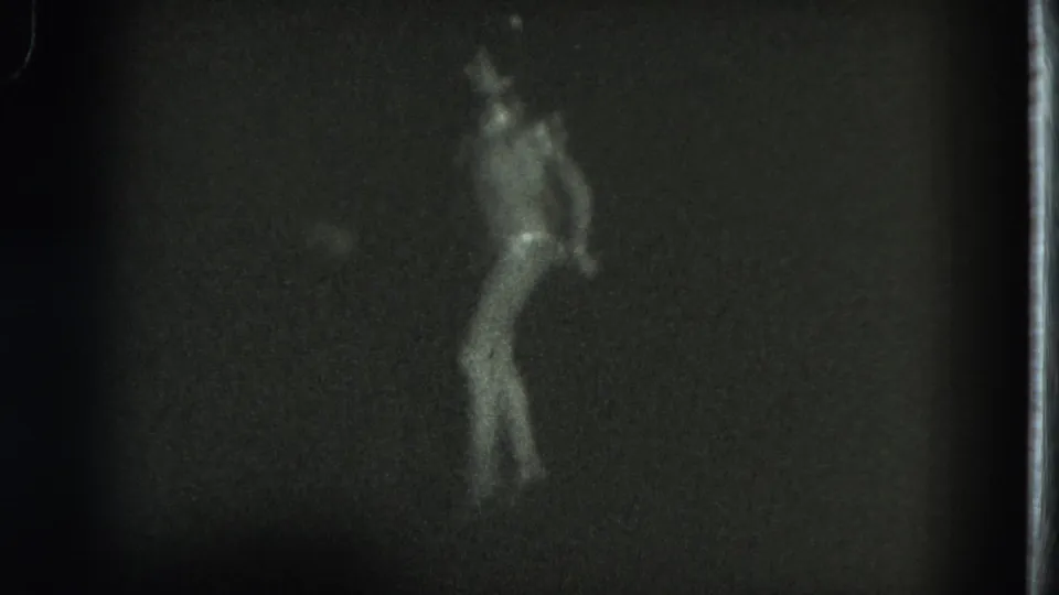 1975 San Francisco 8mm frame showing a female dancer in profile with a feathered headpiece and light costume.