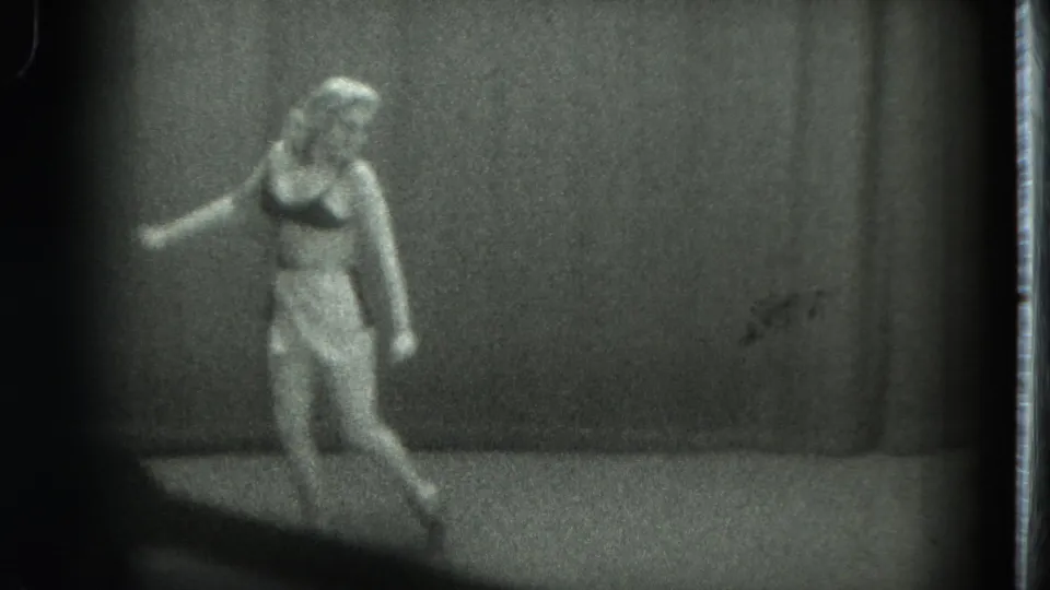 1975 San Francisco 8mm frame showing a woman standing and dancing alone in a softly focused private interior.