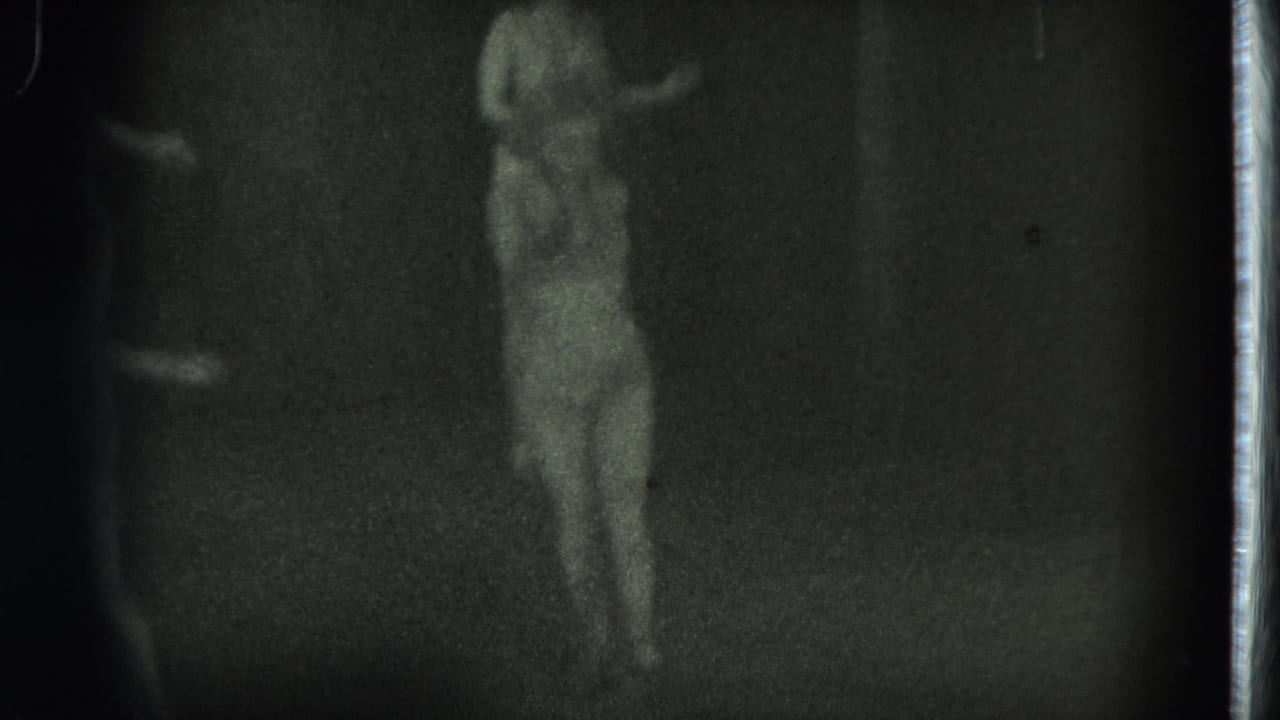 Dancer in a flowing costume standing near the back of a dark stage.
