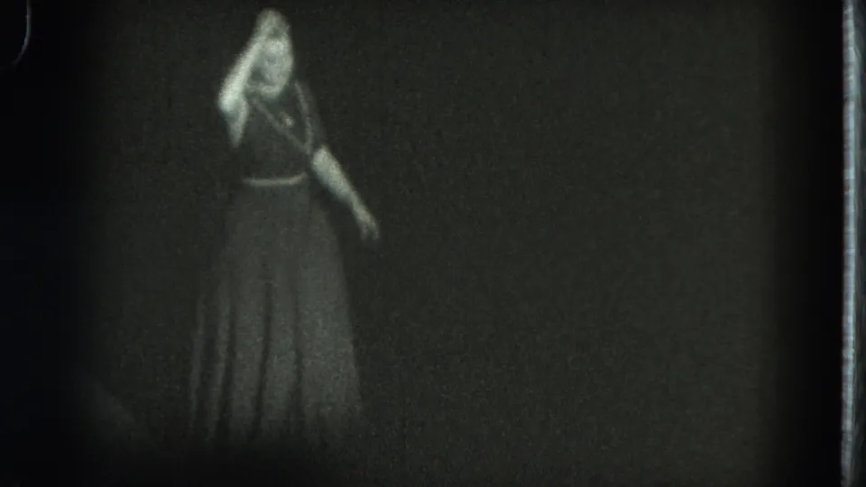 The woman on the dim stage gestures while facing the audience in a grainy 1975 San Francisco 8mm frame.