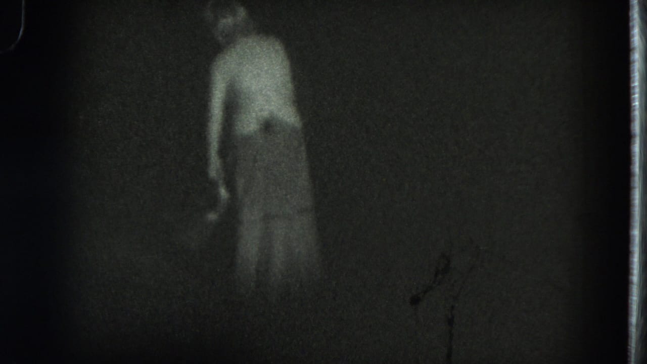 1975 San Francisco 8mm frame showing a woman in a long dress moving through a dark outdoor area at night.
