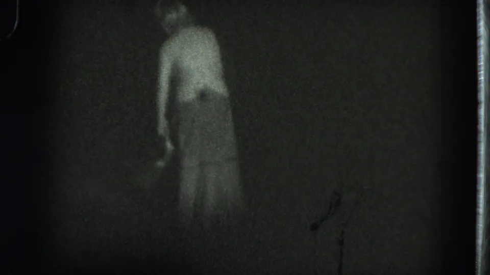 1975 San Francisco 8mm frame showing a woman in a long dress moving through a dark outdoor area at night.