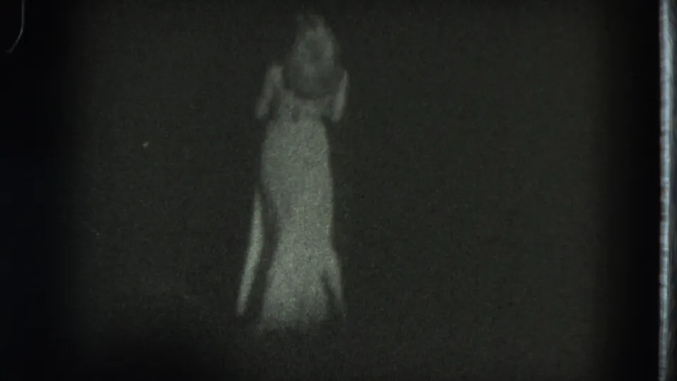 1975 San Francisco 8mm frame showing a woman in a long dress, with fabric appearing blown by wind in the low-light scene.