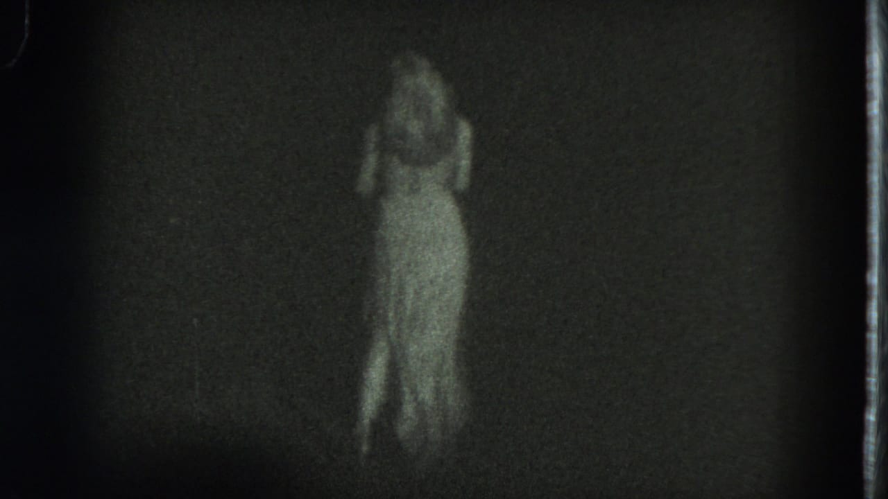 Woman in a pale dress dancing against a dark background.