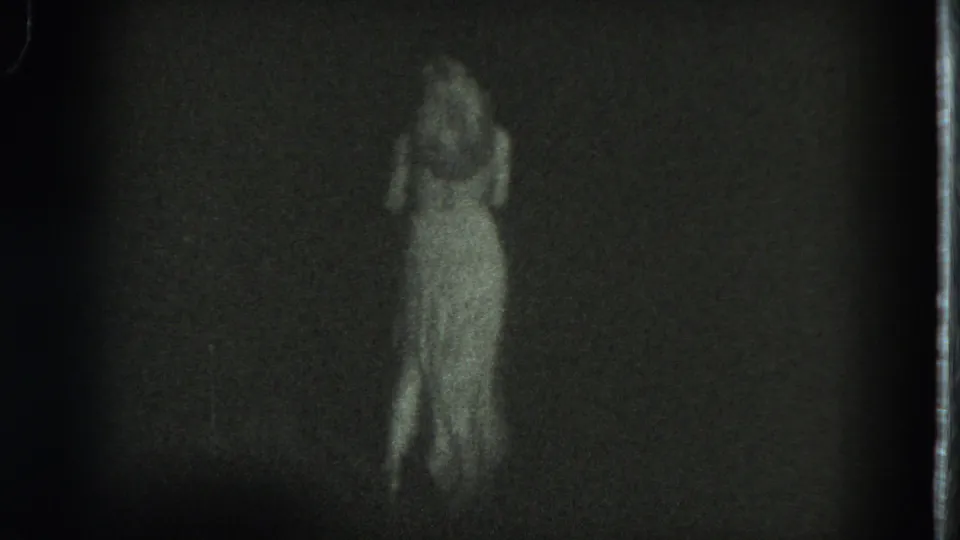 A woman in a flowing white dress appears mid-dance in dim 1975 San Francisco 8mm footage.