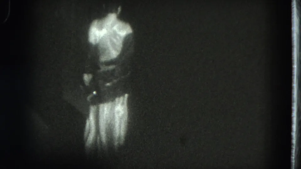 The performer turns away, revealing the back of her long light dress in softly focused 8mm footage from San Francisco in 1975.