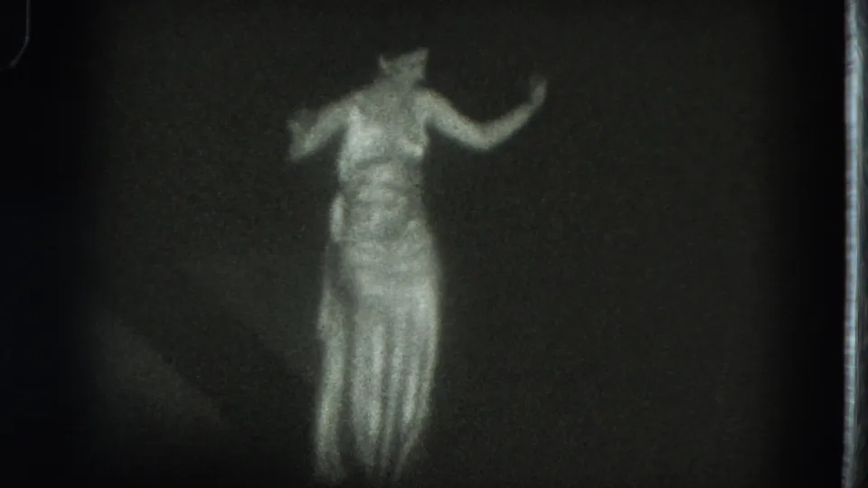 The woman raises one arm in a graceful pose, her long dress glowing against the dark 1975 San Francisco home-movie frame.