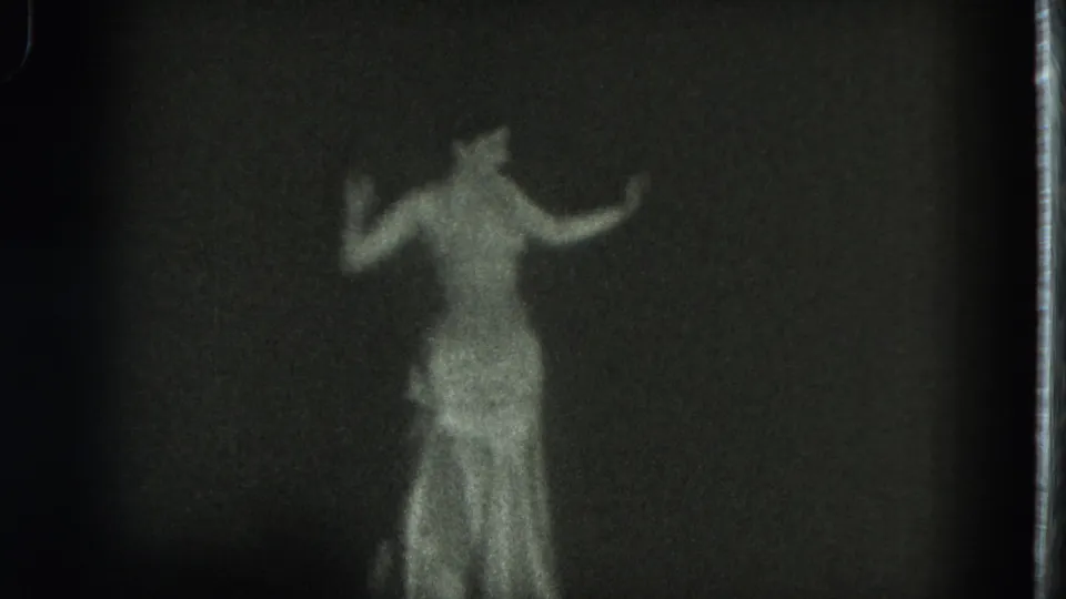 In 1975 San Francisco 8mm footage, a woman in a shimmering gown appears in soft focus while dancing with raised arms.