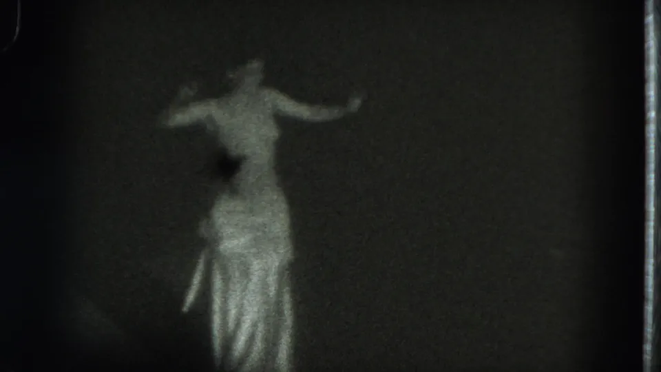 A soft 8mm frame shows the woman dancing in partial profile, with an arm extended and shiny fabric visible at the waist and skirt.
