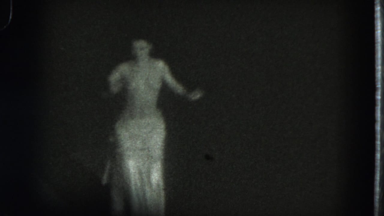 Adult dancer in a flowing skirt seen from behind against a dark background.