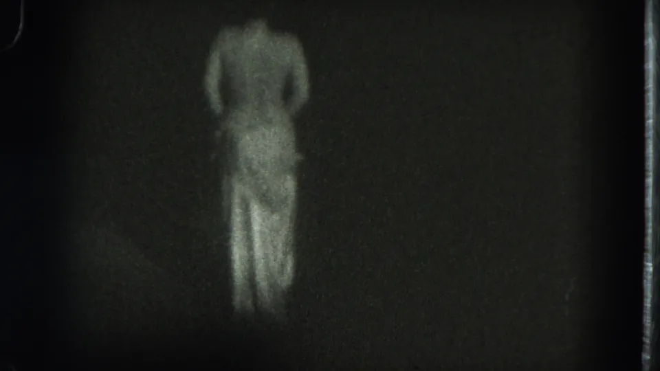 The adult dancer is centered with back to camera, skirt visible, in dim black-and-white 8mm footage from the San Francisco clip.