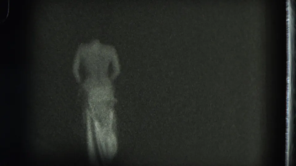 1975 San Francisco 8mm frame showing a topless adult woman from behind in a light skirt, softly blurred by motion and grain.