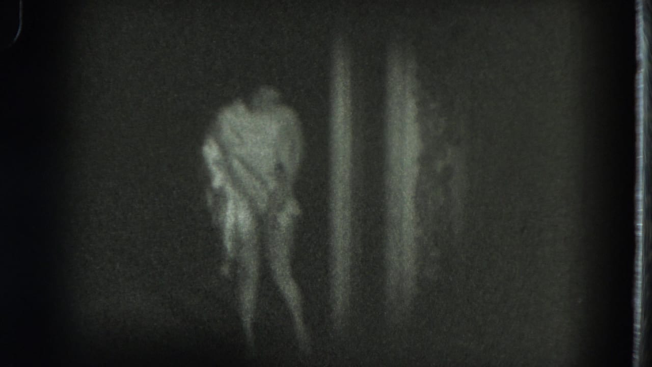 In 1975 San Francisco 8mm footage, a woman in a light dress appears to bow in a dim space, softened by grain and motion blur.