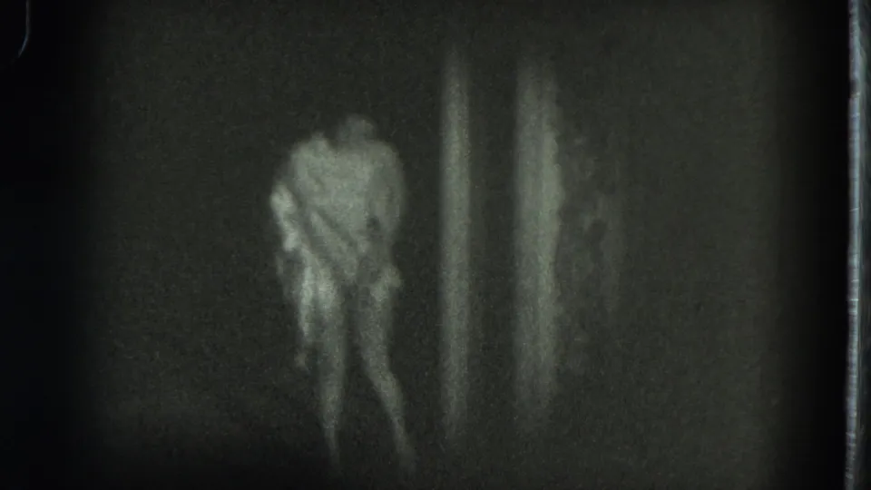 In 1975 San Francisco 8mm footage, a woman in a light dress appears to bow in a dim space, softened by grain and motion blur.